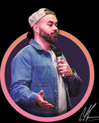 Craig Abbott talking into a microphone at a conference. He is a white male with a short black beard, wearing a denim shirt and a backwards baseball cap.
